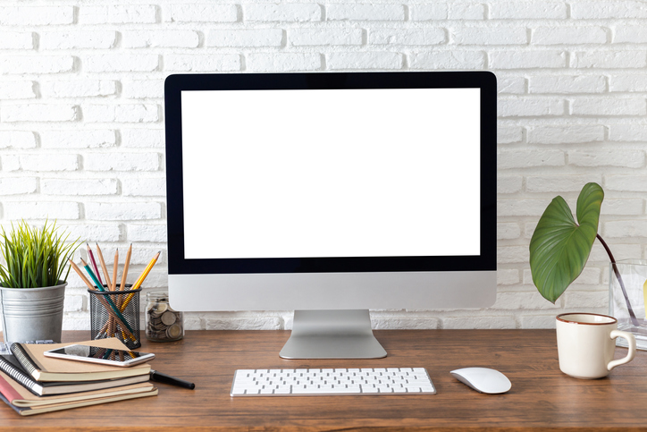 workspace with computer with blank white screen, and office supplies on a wooden desk